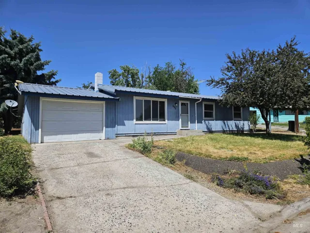 Ranch-style home featuring an attached garage, a metal roof, concrete driveway, and a front lawn