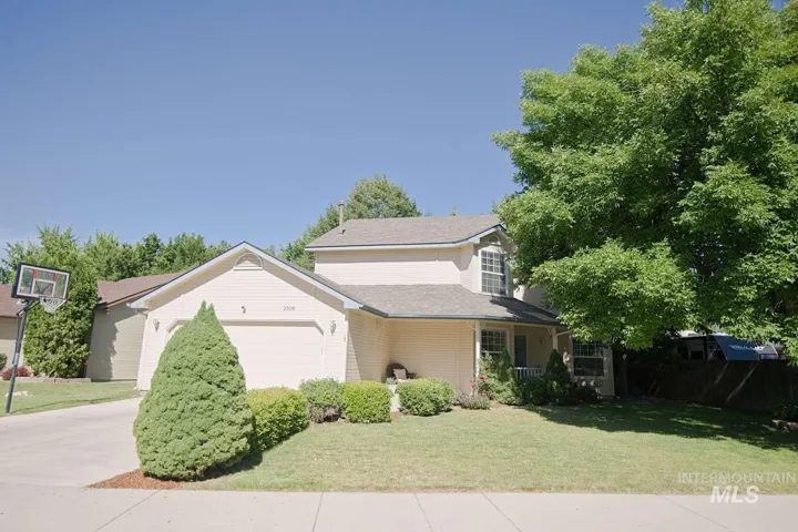 Two-story residence featuring a front lawn with mature landscaping, an attached two-car garage, and a covered porch entry
