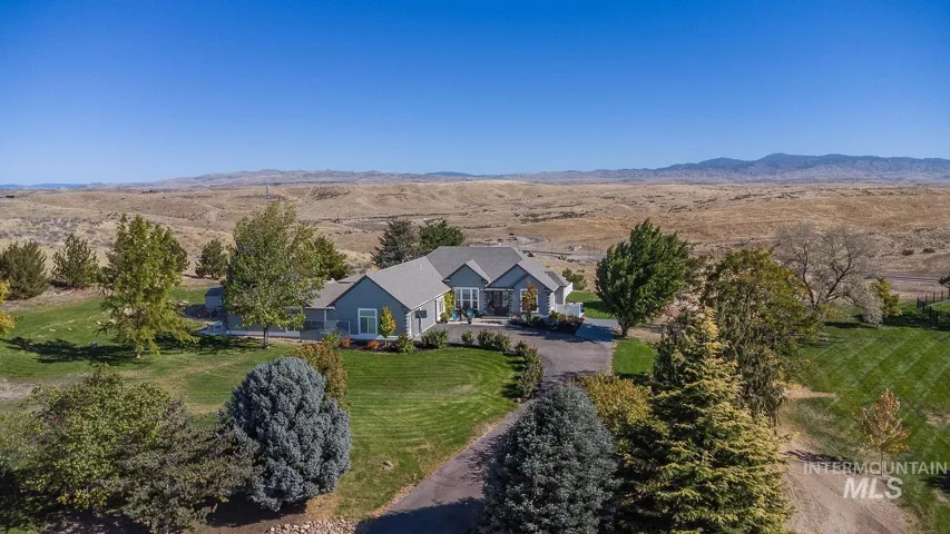 Single-story residence featuring a gray exterior, multi-pitched roofline, paved driveway, expansive lawn, and mountain backdrop