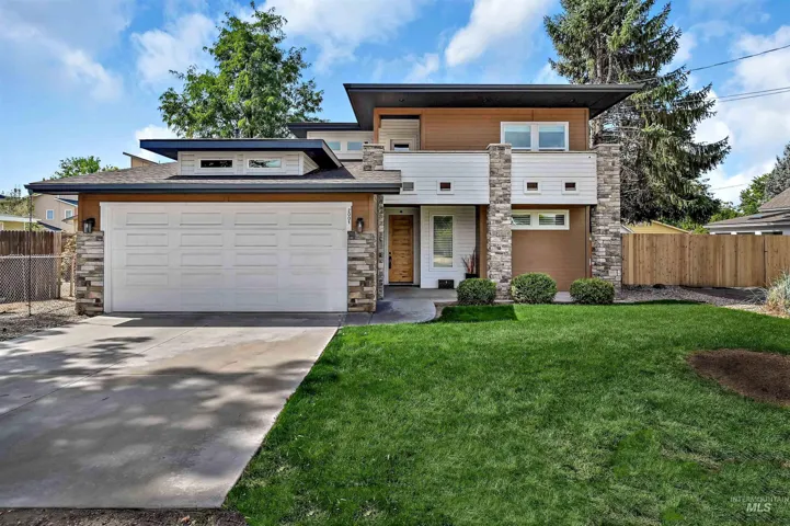 View of front of house with stone siding, concrete driveway, a balcony, and a shingled roof