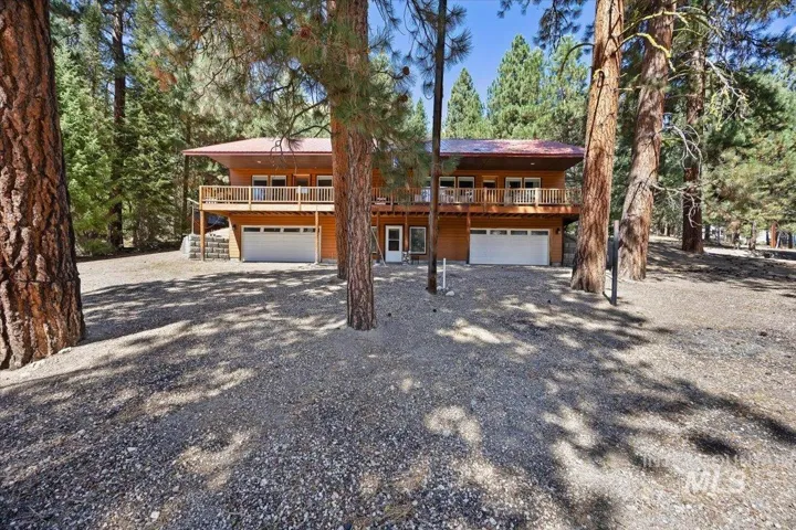 Cedar-clad exterior with a rust-colored metal roof, featuring a full-width upper-level balcony with white railings, and two ground-level garage doors