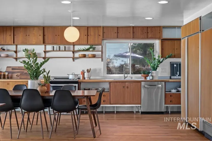 Wood-finish flooring, full-height wood cabinetry, stainless steel dishwasher, integrated refrigerator, and a kitchen window with outdoor scenery