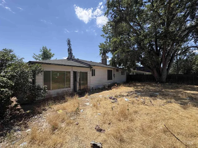 Rear exterior with an expansive dry grass yard, mature trees, and a partial privacy fence
