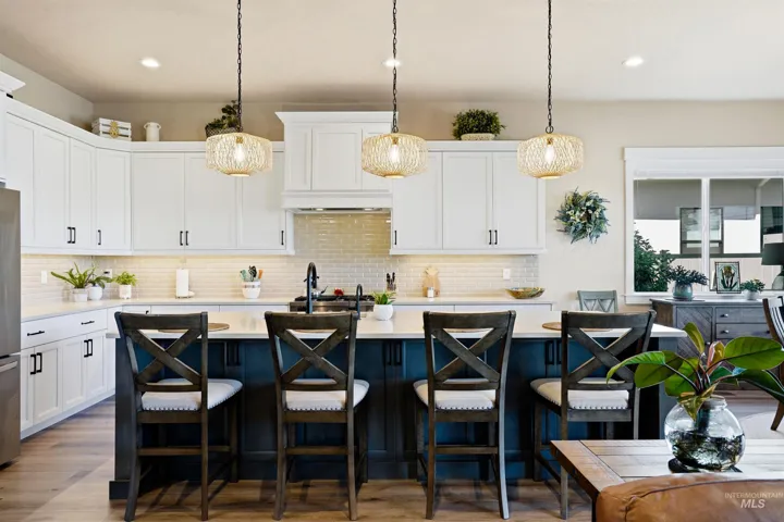 Kitchen featuring white shaker-style cabinetry, a contrasting dark-toned kitchen island, subway tile backsplash, and three woven pendant lights