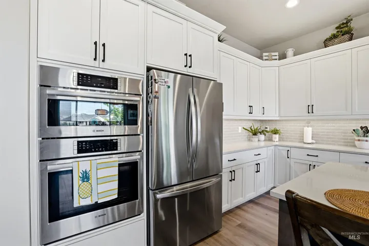 Kitchen featuring white shaker-style cabinetry, stainless steel built-in double ovens, quartz countertops, a brick-patterned tile backsplash, and wood-finish flooring