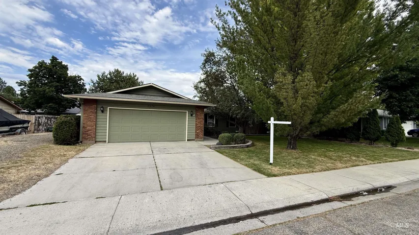 Ranch-style exterior featuring a green siding and brick facade, a two-car garage, concrete driveway, and mature landscaping