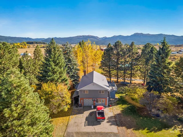 Multi-level exterior featuring a metal roof, concrete driveway, attached garage, and prominent mountain backdrop surrounded by mature coniferous and deciduous trees