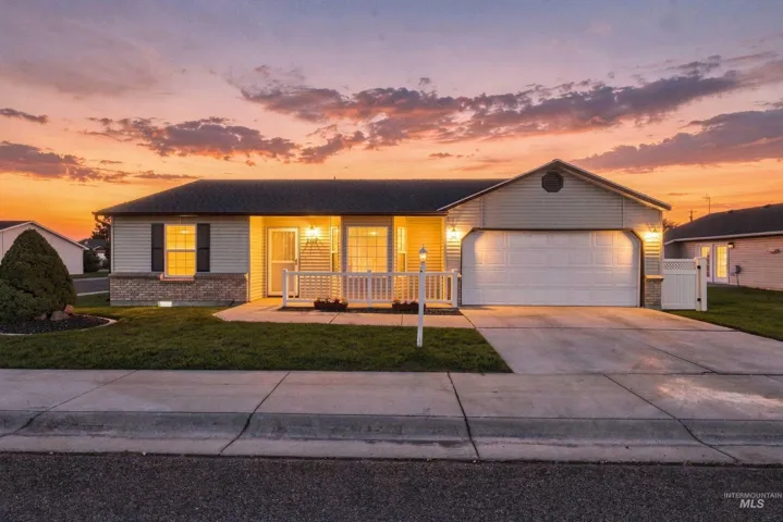 Single-story residence featuring light-colored siding, a covered entry with white railings, a front-facing garage, and a concrete driveway