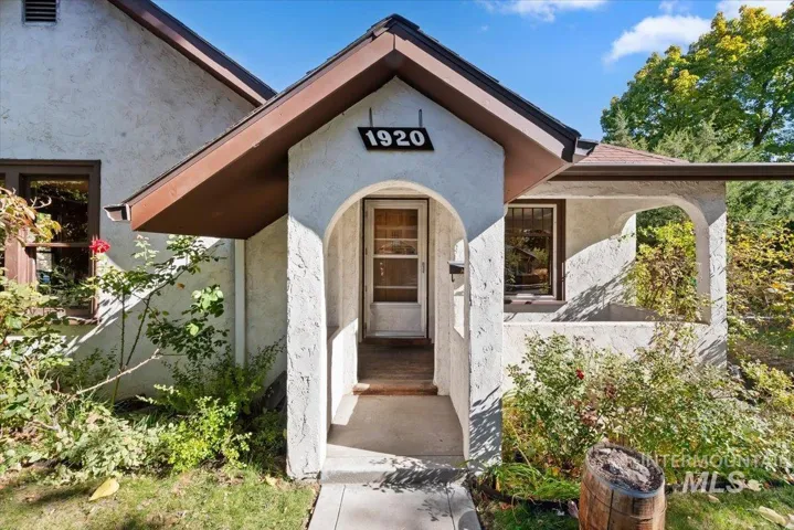 Stucco exterior featuring a covered entryway with an arched opening, a gabled roofline, and a concrete walkway