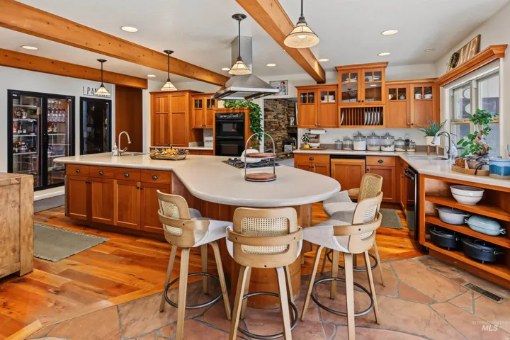 Spacious kitchen featuring exposed wood beams, wood-finish flooring, custom wood cabinetry, a large kitchen island with seating, and a built-in double oven
