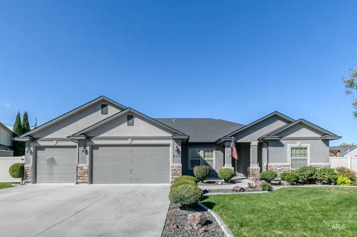 Stucco exterior with stone accents, dark shingles, an attached three-car garage, concrete driveway, and established landscaping