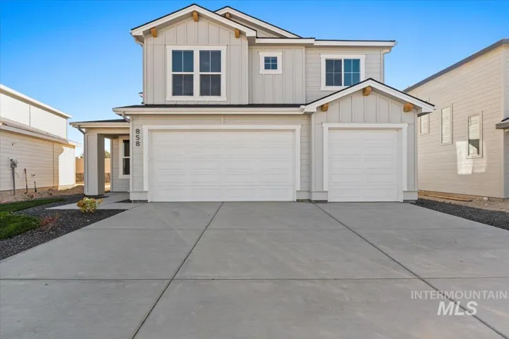 Two-story exterior featuring board and batten siding, decorative wooden gable brackets, a concrete driveway, and a three-car garage
