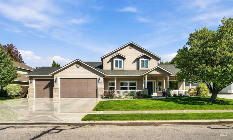 Two-story exterior featuring tan horizontal siding, stone veneer accents, an attached three-car garage, a covered front porch with white railing, and a gabled roofline
