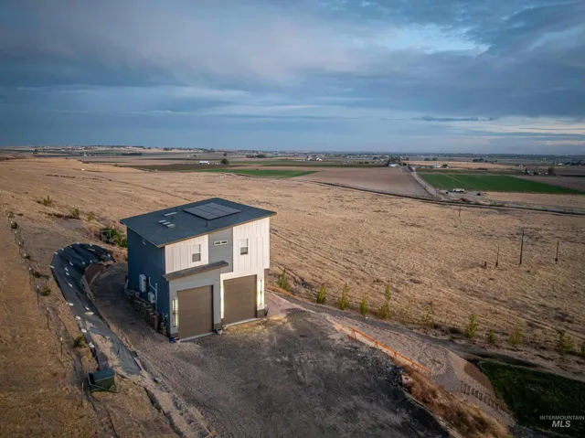 Contemporary two-story structure featuring a dual-tone vertical metal and composite exterior, integrated rooftop solar panels, and dual oversized garage bays