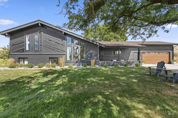 Contemporary exterior with dark siding and brick accents, expansive lawn, multi-pane windows, and a wood-tone garage door