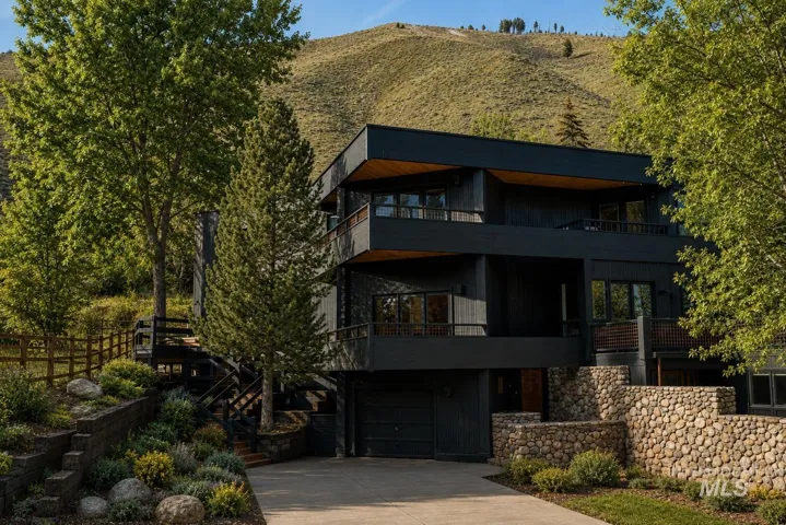 Modern multi-level exterior with dark siding, multiple balconies, a built-in garage, and extensive stone retaining walls