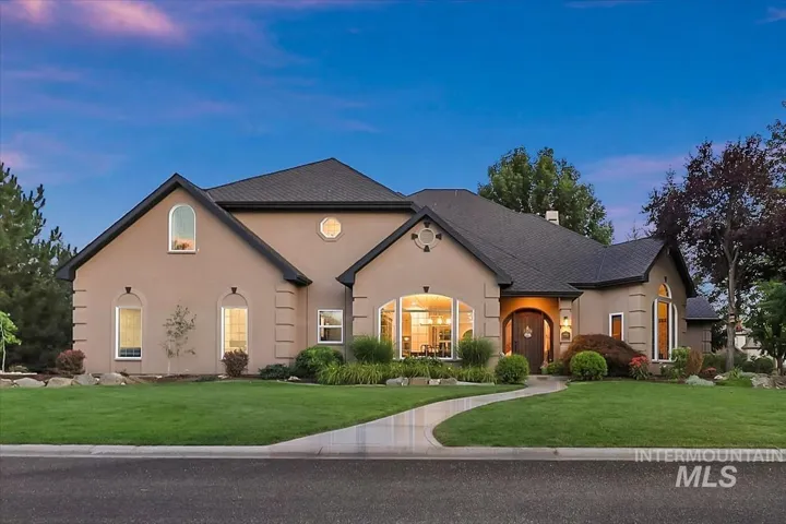 Stucco exterior residence featuring a dark shingle roof and a curved concrete pathway