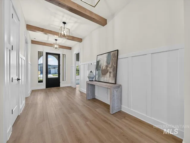 Vaulted ceiling featuring exposed wood beams, wood-finish flooring, board and batten wall detailing, and a black arched entry door with sidelights