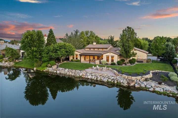 Stucco exterior with a tile roof, covered patio, stone fire pit area, rock-lined water feature, and extensive landscaping
