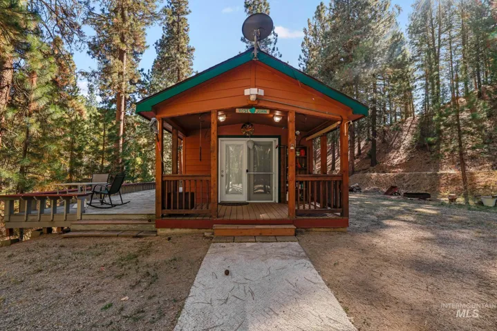 Cabin exterior featuring horizontal wood siding, a covered front porch with railings, and an expanded wraparound wood deck