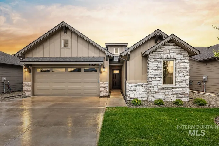 Exterior facade featuring vertical siding, stone masonry accents, a gabled roofline with decorative corbels, and an attached multi-car garage