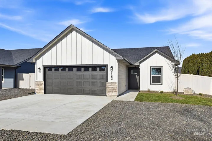 Contemporary single-story residence featuring white vertical and horizontal siding, a dark gray garage door, and stone facade accents